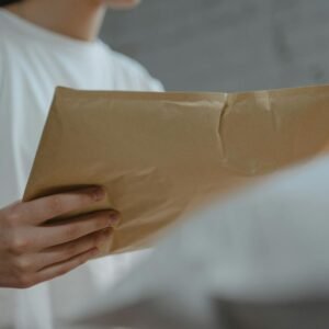 Close-up of a person holding a brown paper envelope, highlighting courier services or postal delivery indoors.