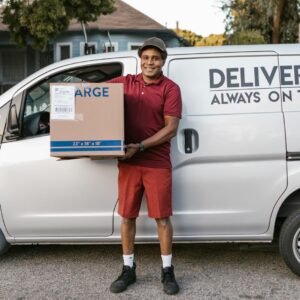 A courier in a maroon uniform smiling with a package in front of a delivery van.
