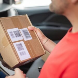 Close-up of a person holding a package with QR codes inside a car, emphasizing delivery and technology.